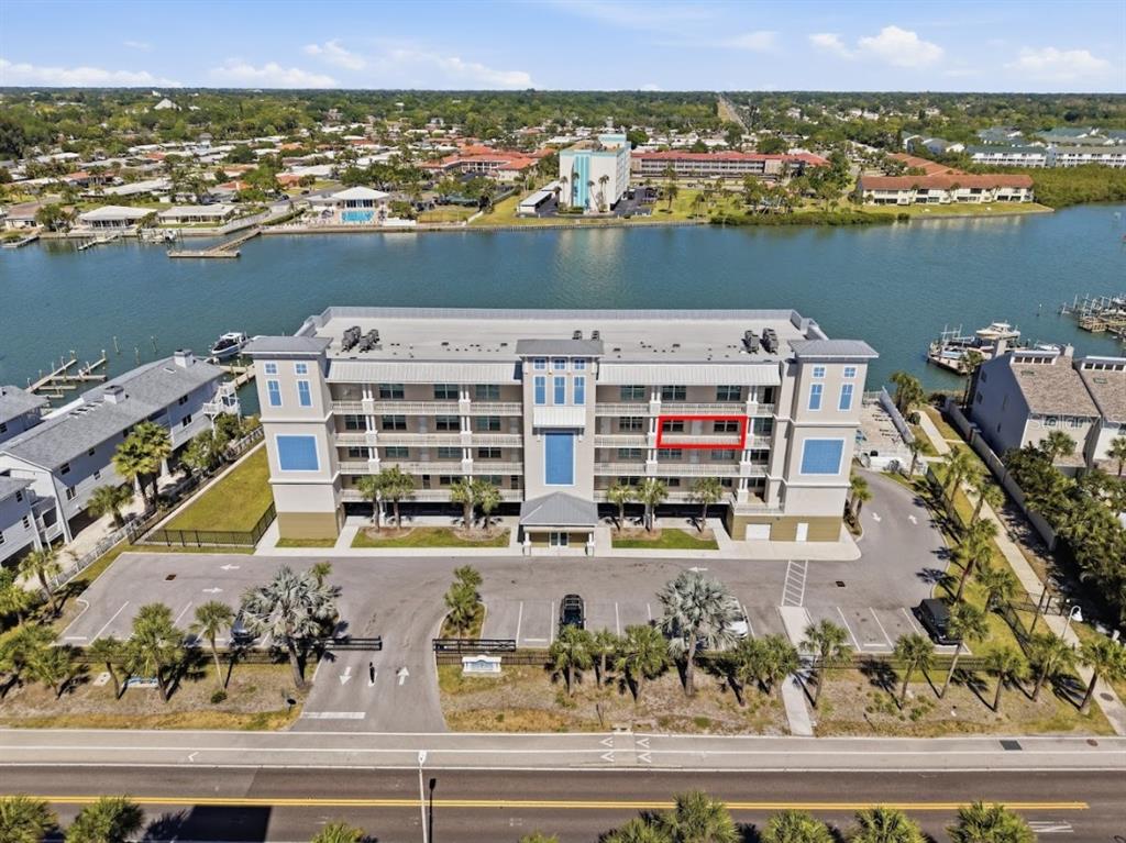 An aerial view shows a multi-story apartment building with a red-outlined balcony facing the water — 20001 GULF BOULEVARD UNIT 405, INDIAN SHORES, FL
