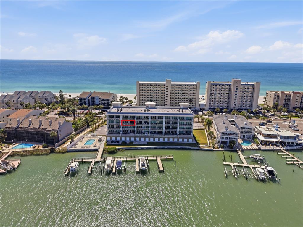 An aerial view shows a multi-story waterfront condominium building with boat docks and a pool — 20001 GULF BOULEVARD UNIT 405, INDIAN SHORES, FL