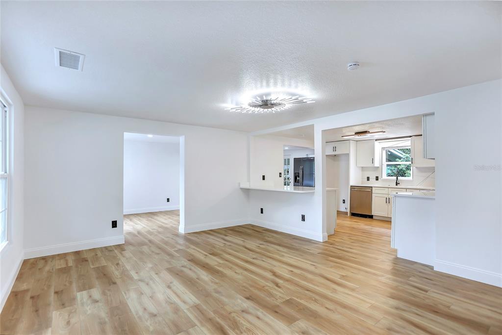 A bright living room with light wood flooring opens into a kitchen with white cabinets — 1920 BAXTER AVENUE, ORLANDO, FL