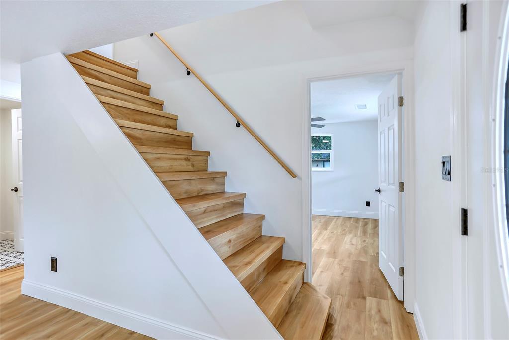 A wooden staircase with a handrail leads upward next to a doorway in a room — 1920 BAXTER AVENUE, ORLANDO, FL