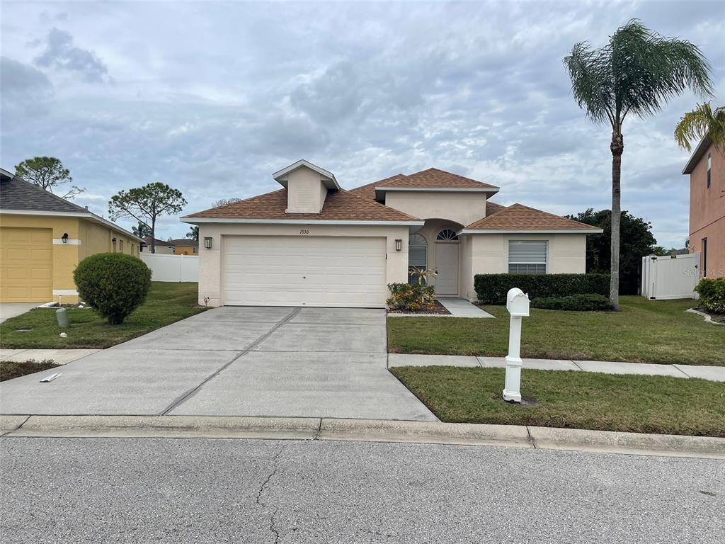A single-story house with a beige stucco exterior, a two-car garage, and a palm tree — 1530 OCEAN REEF ROAD, WESLEY CHAPEL, FL