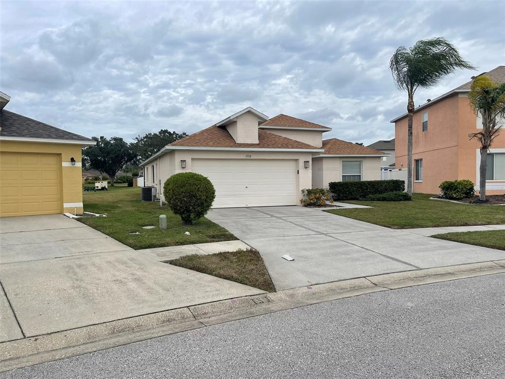 A single-story suburban house with a tan exterior, a two-car garage, and a concrete driveway — 1530 OCEAN REEF ROAD, WESLEY CHAPEL, FL