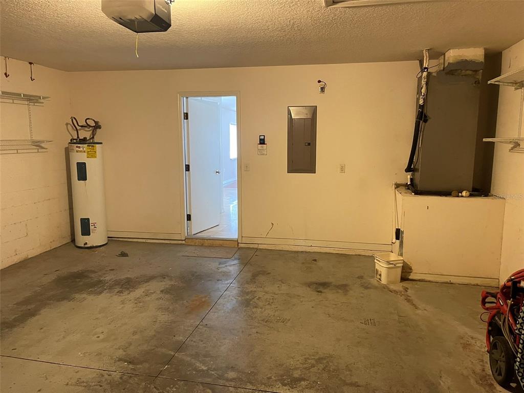 A garage interior featuring a water heater, electrical panel, and an open doorway to inside — 1530 OCEAN REEF ROAD, WESLEY CHAPEL, FL