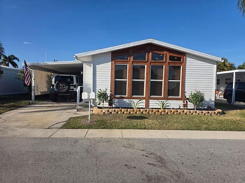 A white manufactured home with a carport, wood-trimmed windows, and a small stone garden bed — 4300 SE Saint Lucie Boulevard # 70, Stuart FL 34997, STUART, FL