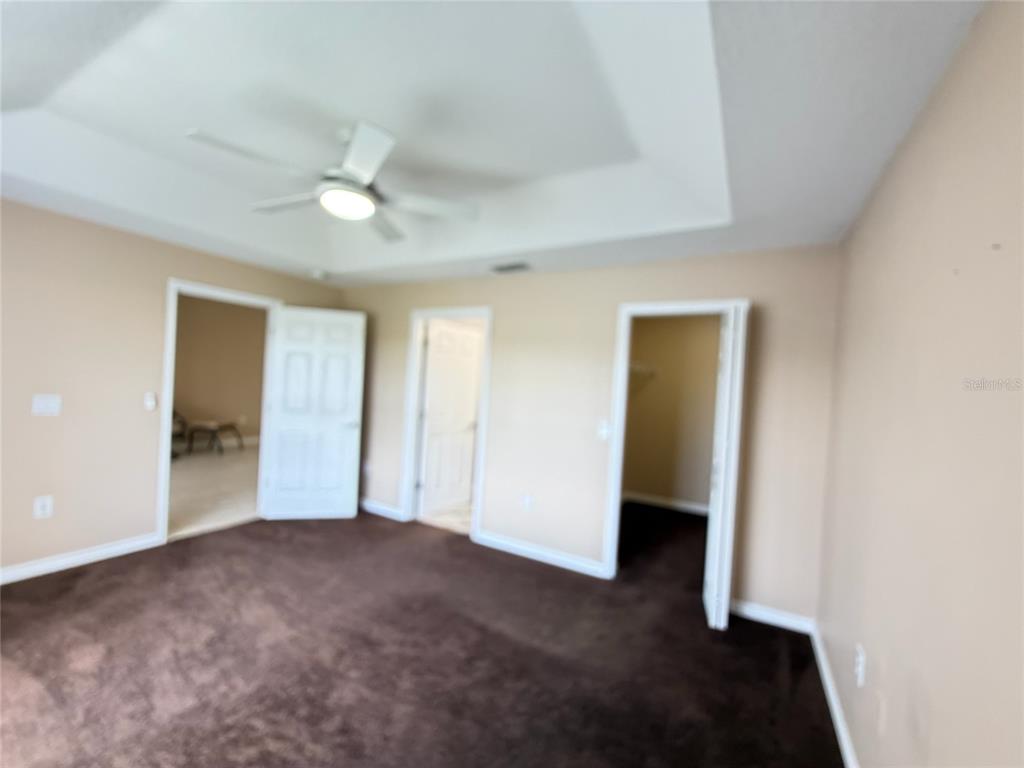 A bedroom with brown carpet, a tray ceiling with a fan, and three open doorways — 315 EAGLE RIDGE ROAD, DAVENPORT, FL