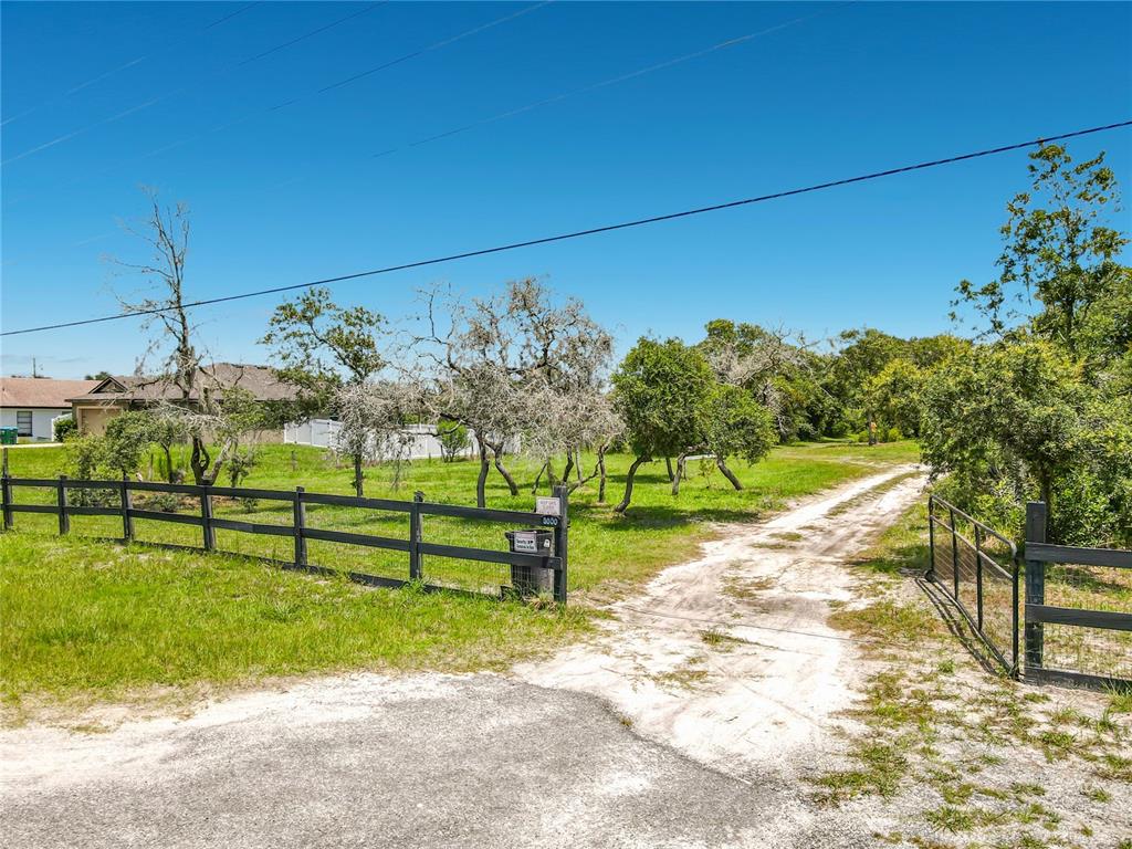 A dirt driveway leads through an open gate into a grassy lot with scattered trees — 3000 LOCKWOOD BOULEVARD, DELTONA, FL