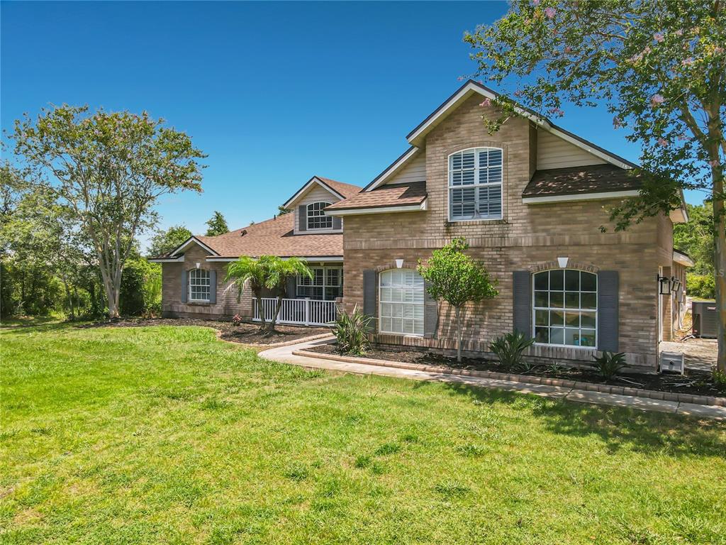 A two-story brick house with a front lawn, walkway, and trees under a blue sky — 3000 LOCKWOOD BOULEVARD, DELTONA, FL