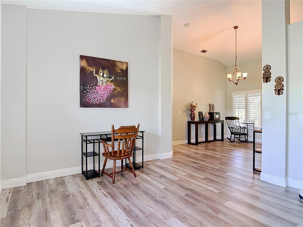 A room with light wood-look flooring, a desk with a wooden chair, and an adjacent dining area — 3000 LOCKWOOD BOULEVARD, DELTONA, FL