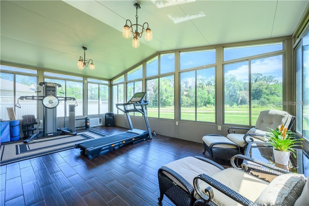 A sunroom with dark wood-look tile flooring, exercise equipment, and wicker seating overlooking a lawn — 105 CEDAR HEIGHTS COURT, SANFORD, FL