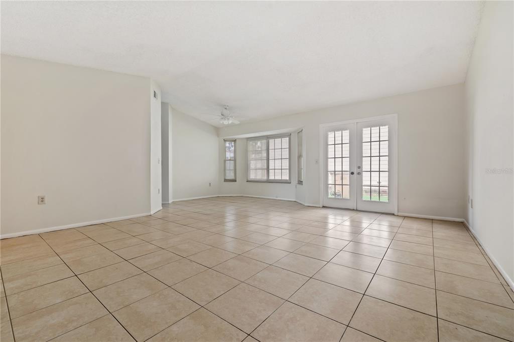 An empty living room features light-colored tile flooring, white walls, a ceiling fan, and French doors — 7607 GLADES COURT, TAMPA, FL