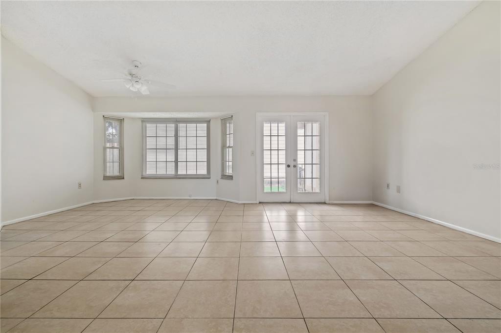 An empty room with beige tile flooring, a ceiling fan, a bay window, and French doors — 7607 GLADES COURT, TAMPA, FL