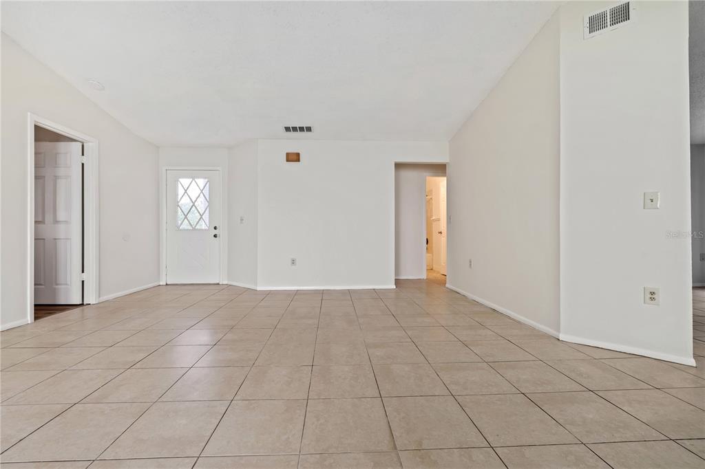 An empty room with beige tile flooring, white walls, a front door, and vaulted ceilings — 7607 GLADES COURT, TAMPA, FL