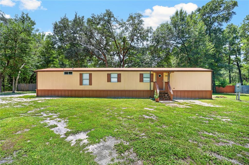 A single-story manufactured home with tan siding and brown trim sits on a grassy lot — 8200 SE 145 STREET, DUNNELLON, FL
