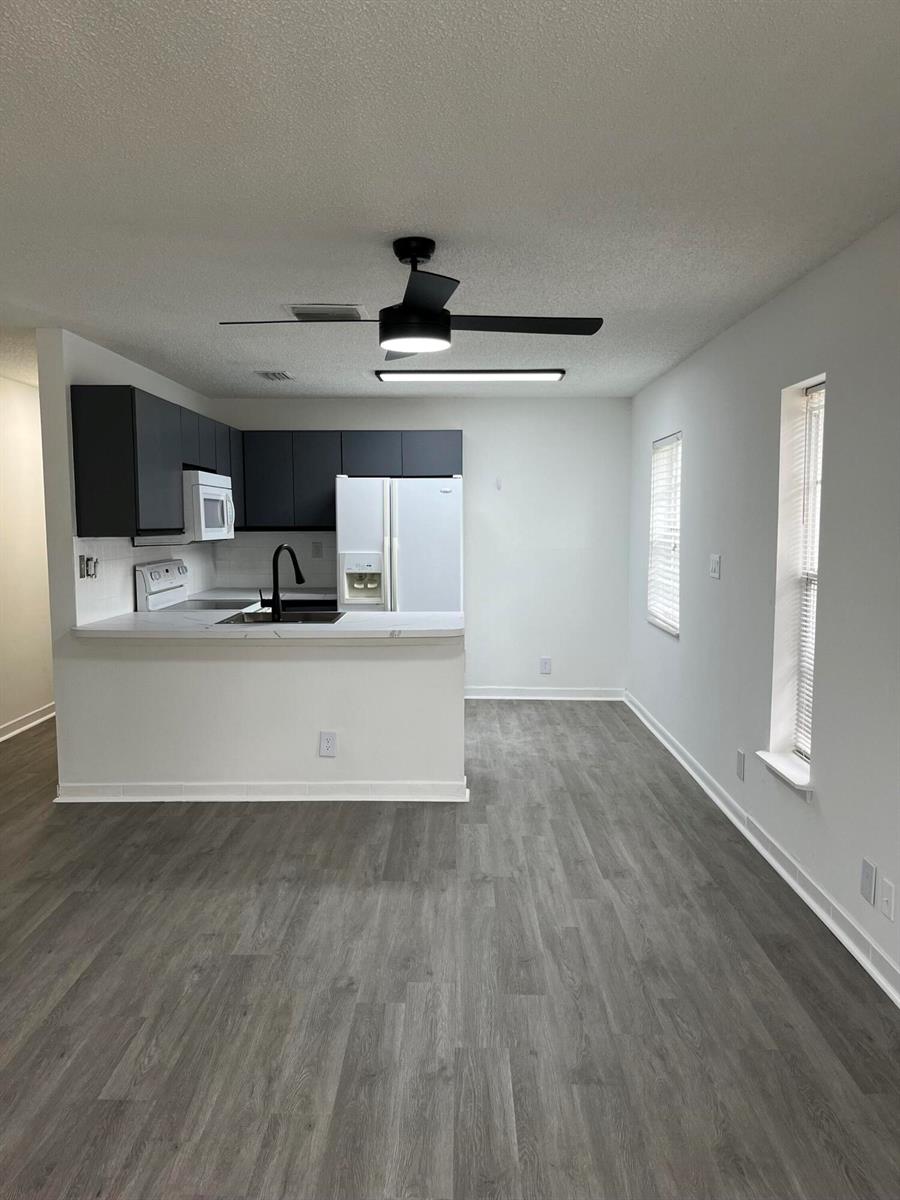 A kitchen with dark cabinets and white appliances overlooks an open dining area with windows — 5665 Boynton Cove Way, Boynton Beach FL 33437, BOYNTON BEACH, FL