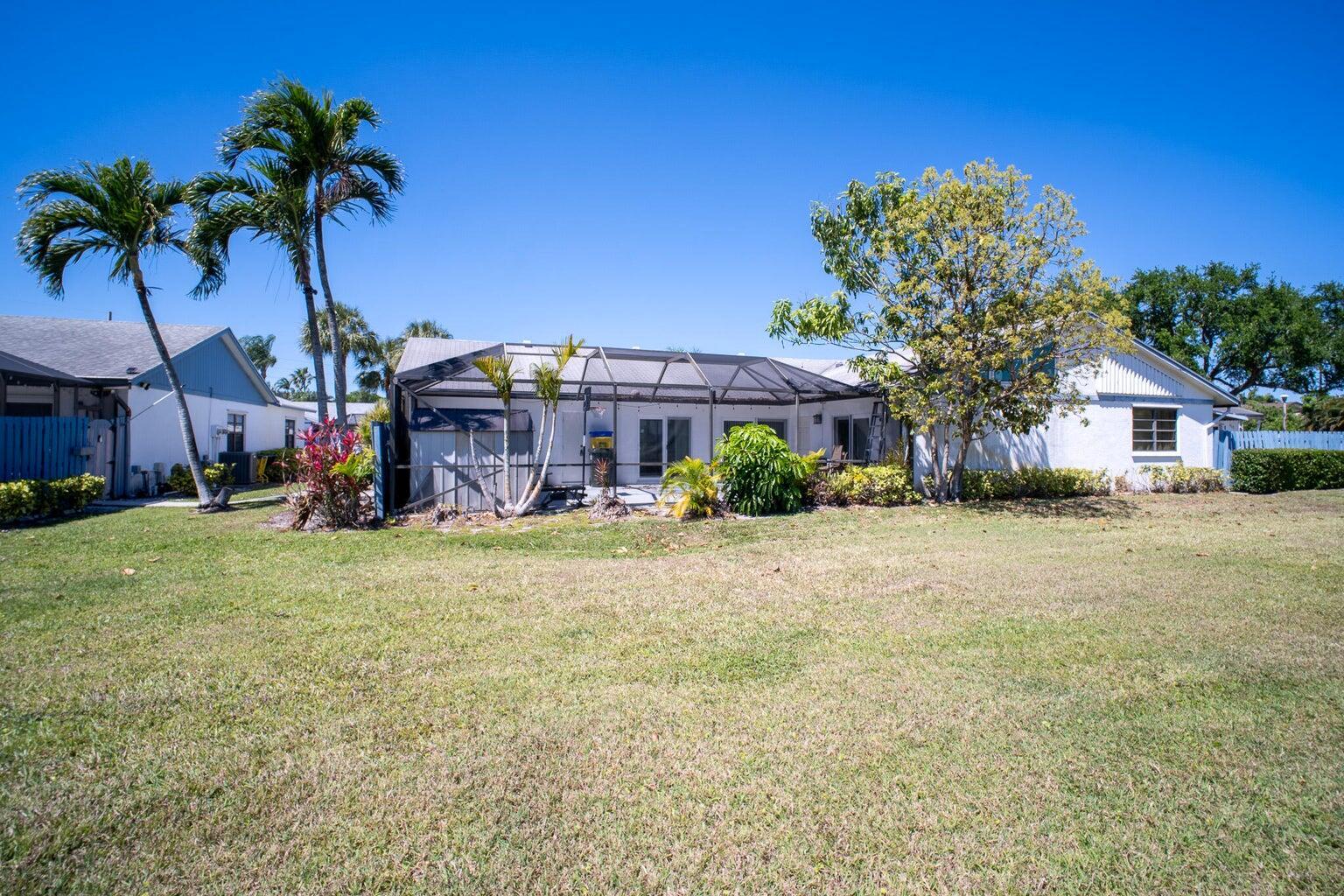 A white house with a screened-in patio sits behind a large, grassy backyard — 1103 Timberlane Circle, FL 33463, FL