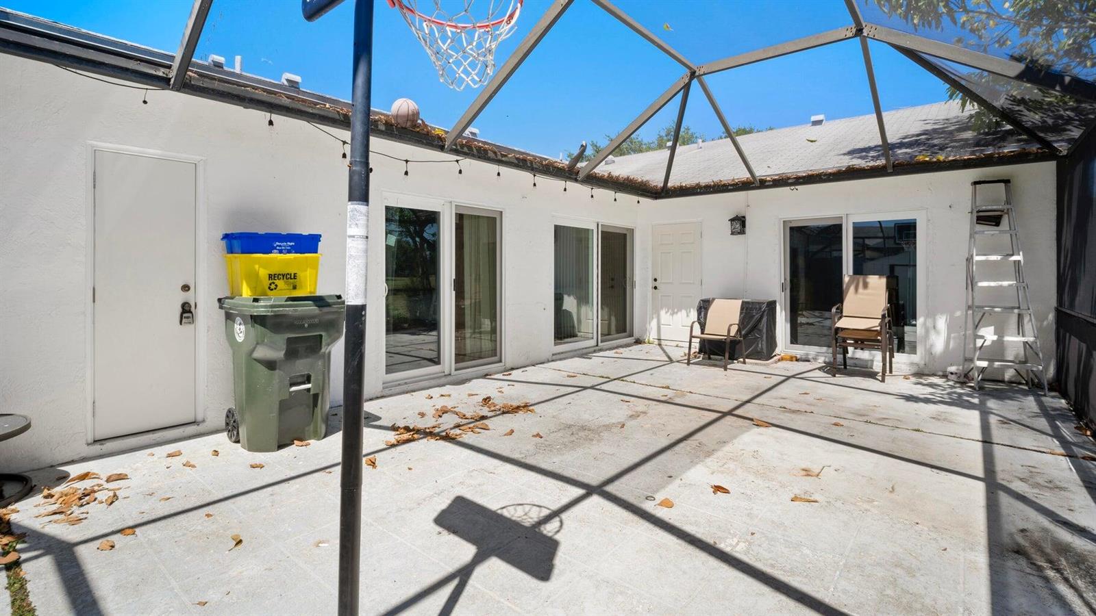 A screened-in concrete patio features a basketball hoop, sliding glass doors, and a storage bin — 1103 Timberlane Circle, FL 33463, FL