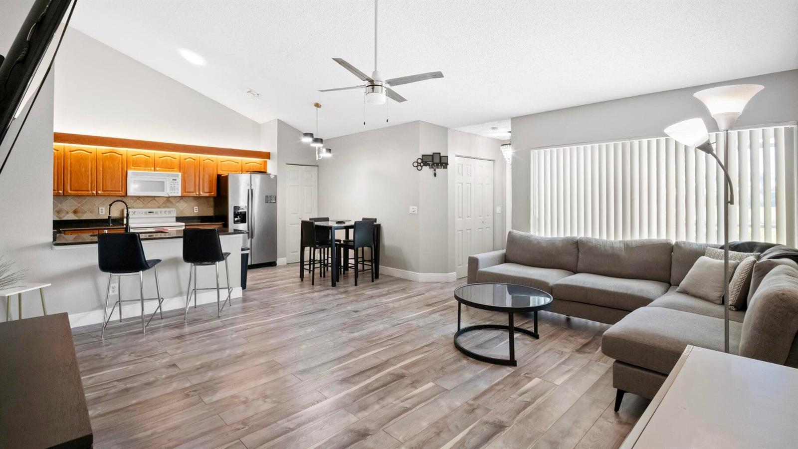 An open-concept living room and kitchen featuring wood-look flooring, gray walls, and a sectional sofa — 1103 Timberlane Circle, FL 33463, FL