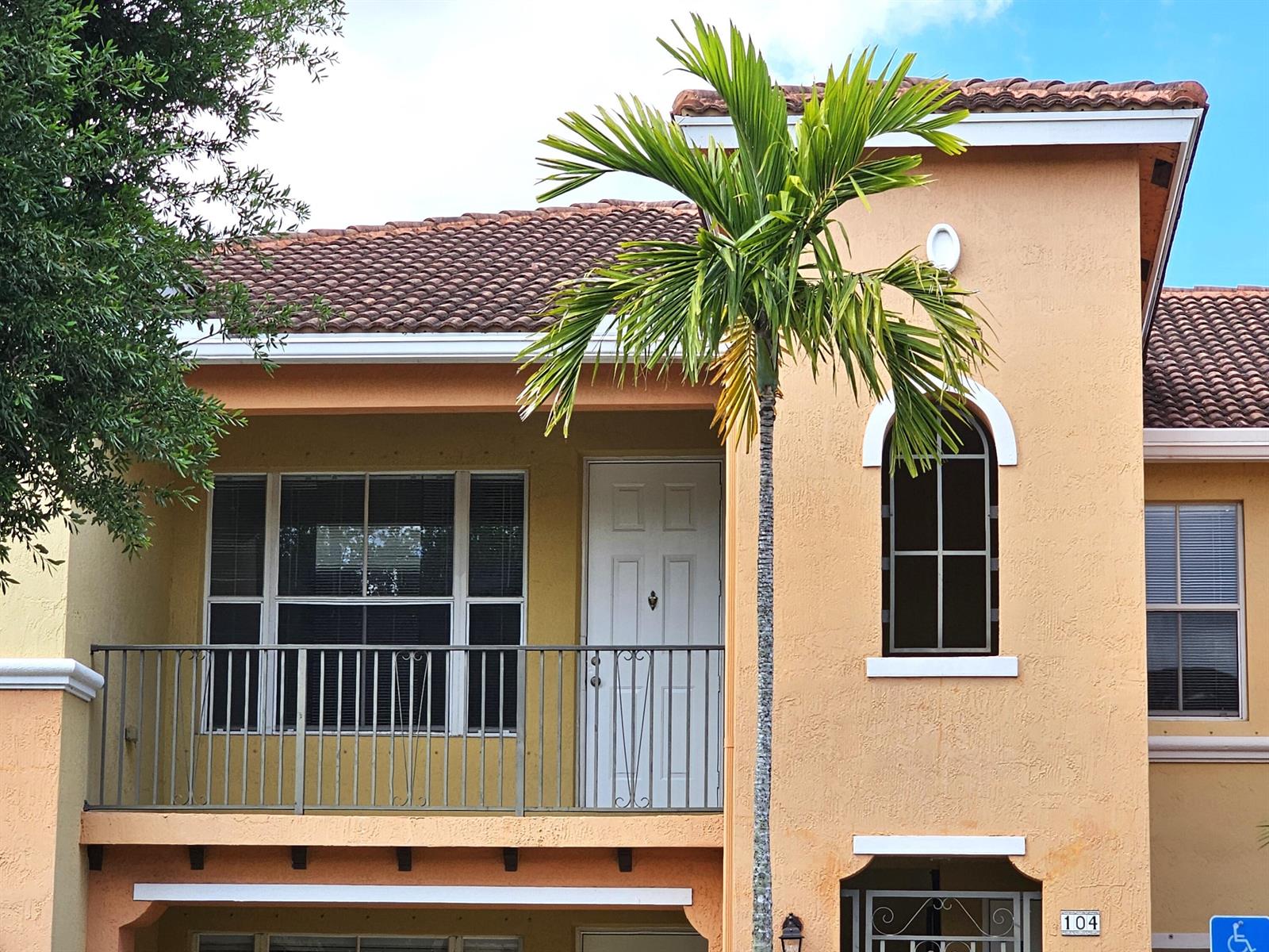 A two-story stucco building features a balcony, a palm tree, and a tiled roof — 3569 Forest Hill Boulevard # 104, Palm Springs FL 33406, PALM SPRINGS, FL