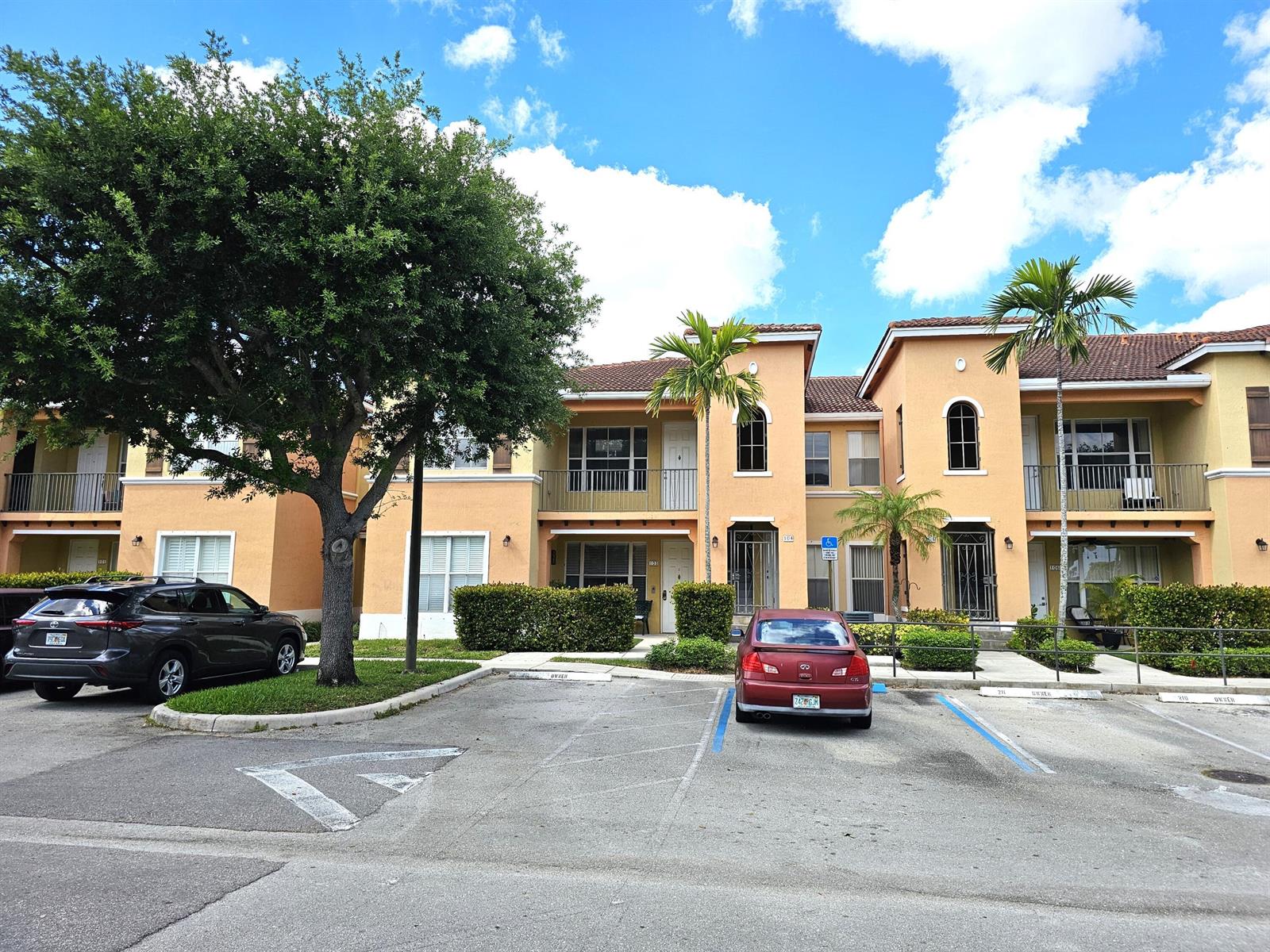 A two-story apartment building with tan stucco walls, a tile roof, and parking spaces — 3569 Forest Hill Boulevard # 104, Palm Springs FL 33406, PALM SPRINGS, FL