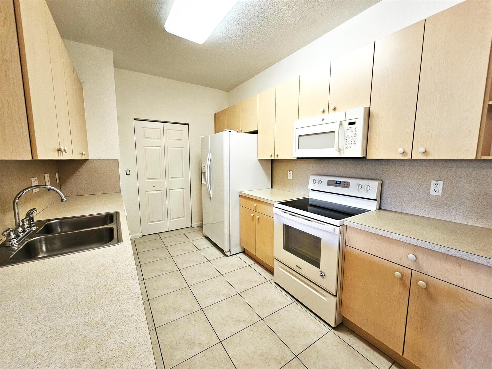 A kitchen features light wood cabinets, white appliances, a double sink, and tiled flooring — 3569 Forest Hill Boulevard # 104, Palm Springs FL 33406, PALM SPRINGS, FL
