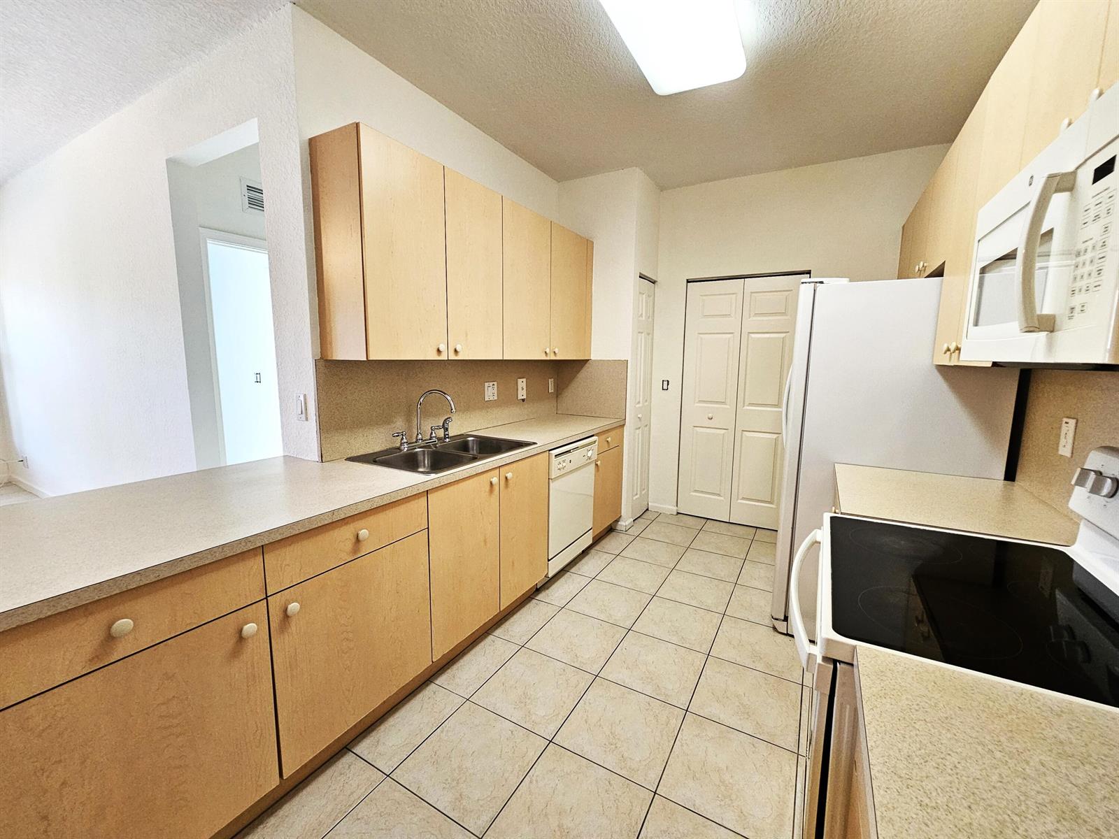A kitchen features light wood cabinets, beige countertops, tile flooring, and white appliances — 3569 Forest Hill Boulevard # 104, Palm Springs FL 33406, PALM SPRINGS, FL