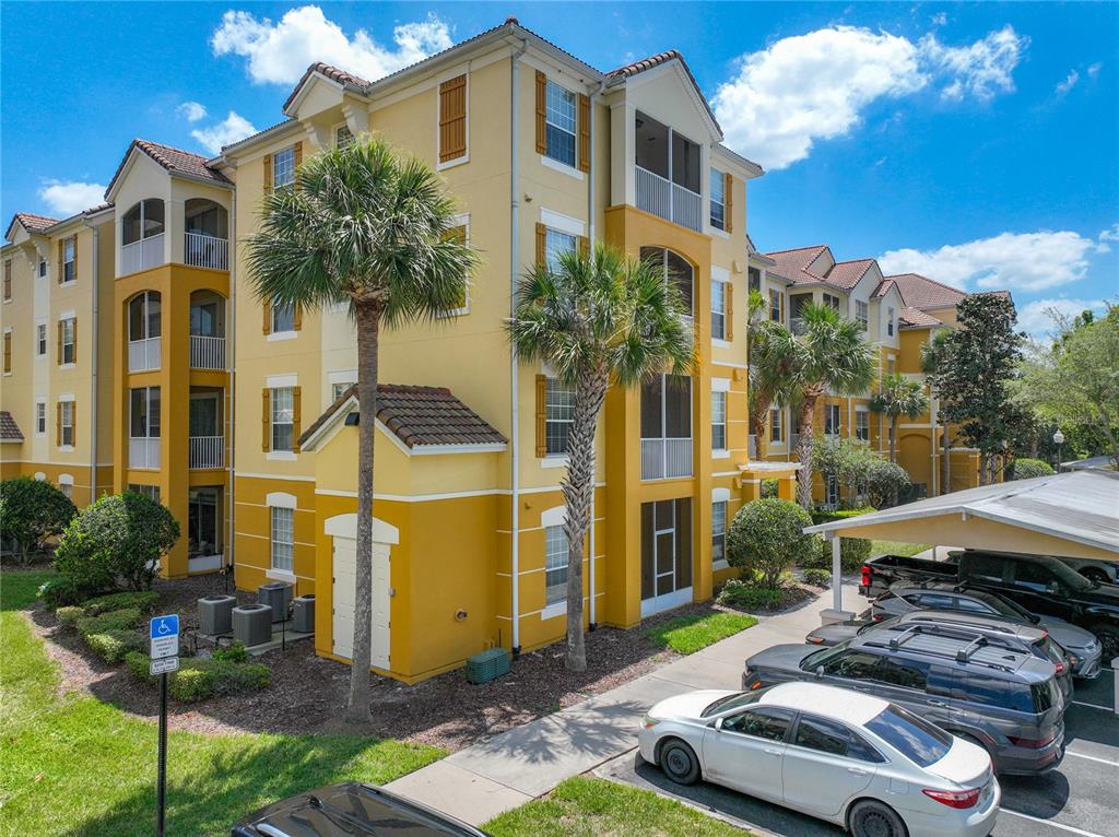 A multi-story yellow apartment building with a parking lot and palm trees in front — 3338 ROBERT TRENT JONES DRIVE UNIT 307, ORLANDO, FL