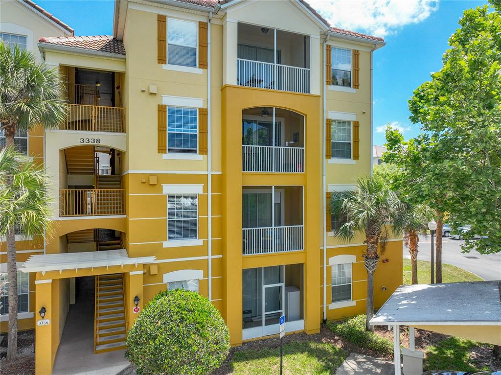 A three-story yellow apartment building features exterior staircases, screened balconies, and a covered parking area — 3338 ROBERT TRENT JONES DRIVE UNIT 307, ORLANDO, FL