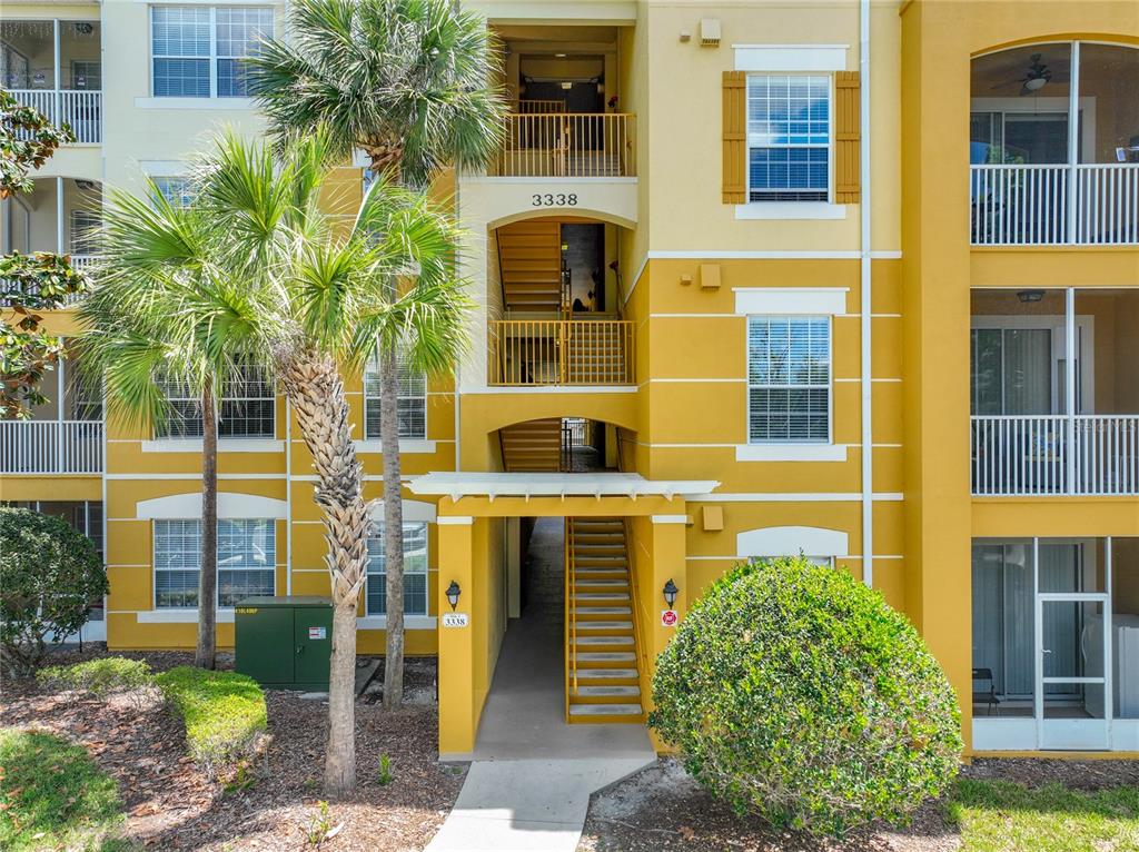 An exterior view of a three-story yellow apartment building with stairs and palm trees — 3338 ROBERT TRENT JONES DRIVE UNIT 307, ORLANDO, FL