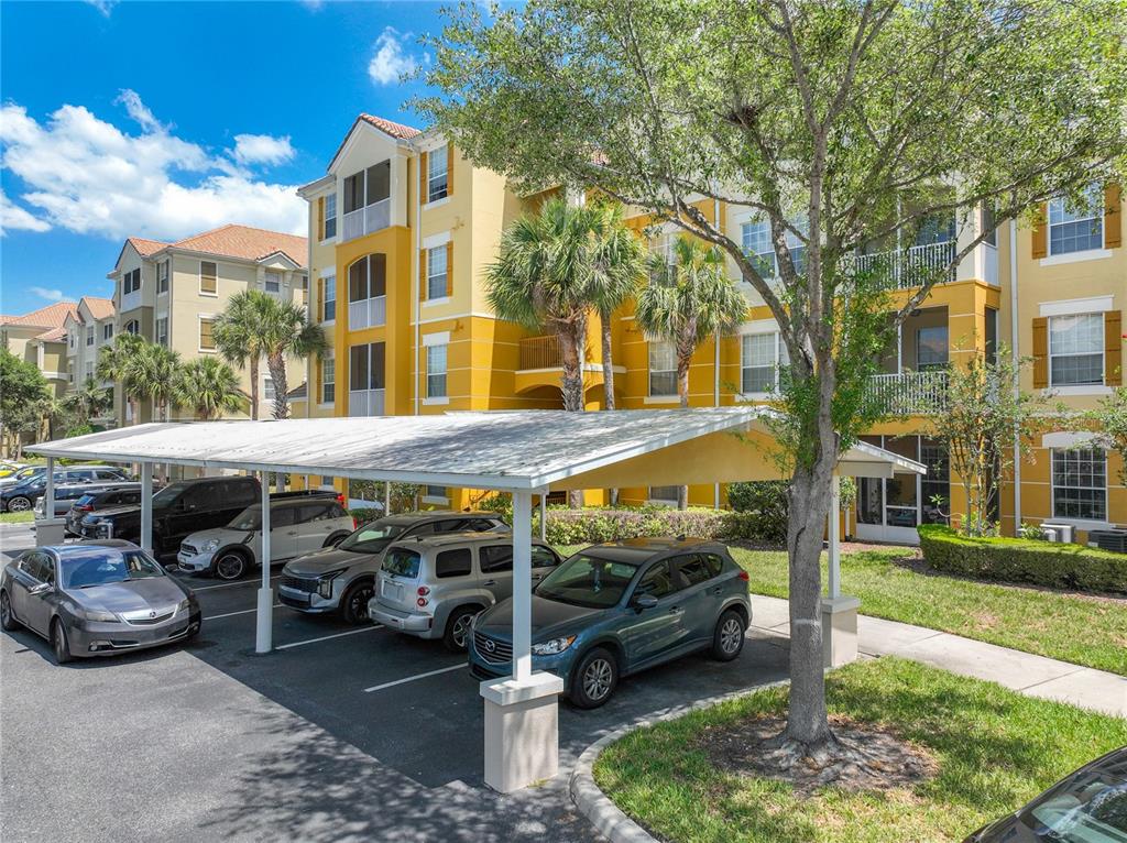 A multi-story yellow apartment building with a covered parking structure in the foreground — 3338 ROBERT TRENT JONES DRIVE UNIT 307, ORLANDO, FL