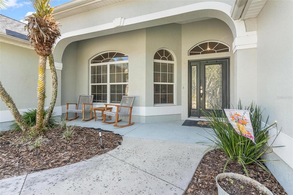A covered front porch features two rocking chairs, a decorative door, and a palm tree — 1027 URICO GOLF ROAD, LADY LAKE, FL