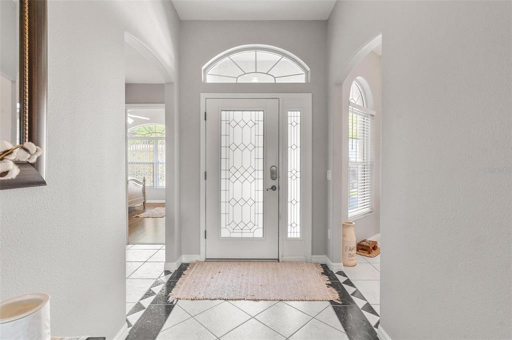 A bright entryway features a glass-paneled front door, arched transom window, and tiled flooring — 1027 URICO GOLF ROAD, LADY LAKE, FL