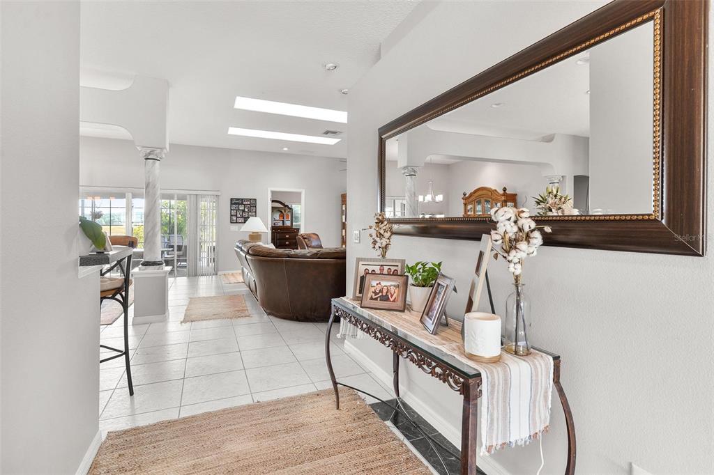 An entryway features a console table with decor, a large wall mirror, and tiled flooring — 1027 URICO GOLF ROAD, LADY LAKE, FL