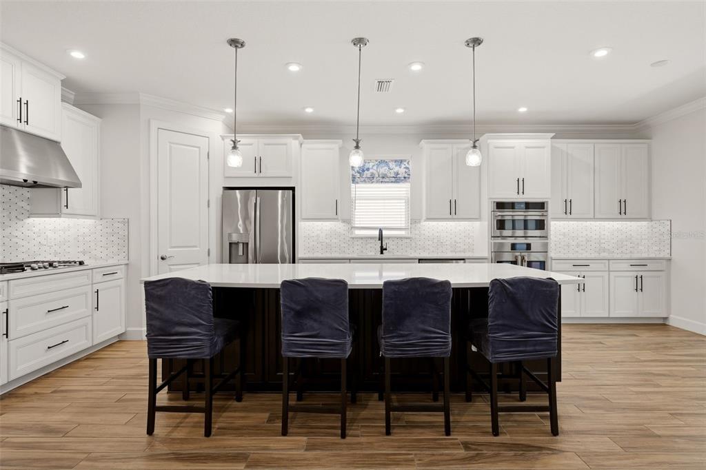 A modern kitchen features white cabinetry, a large dark island with four chairs, and stainless appliances — 10912 SEASONS WAY, PALMETTO, FL