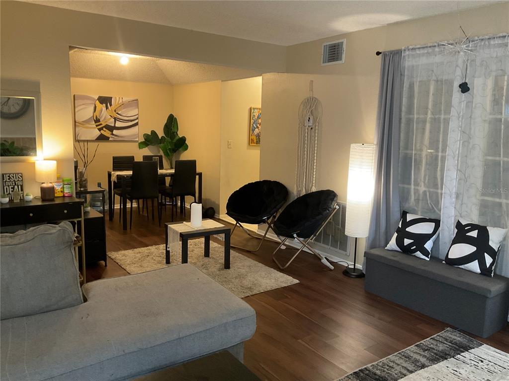 A living room with wood-look flooring flows into a dining area with black chairs — 2197 FOX CHASE BOULEVARD UNIT 101, PALM HARBOR, FL