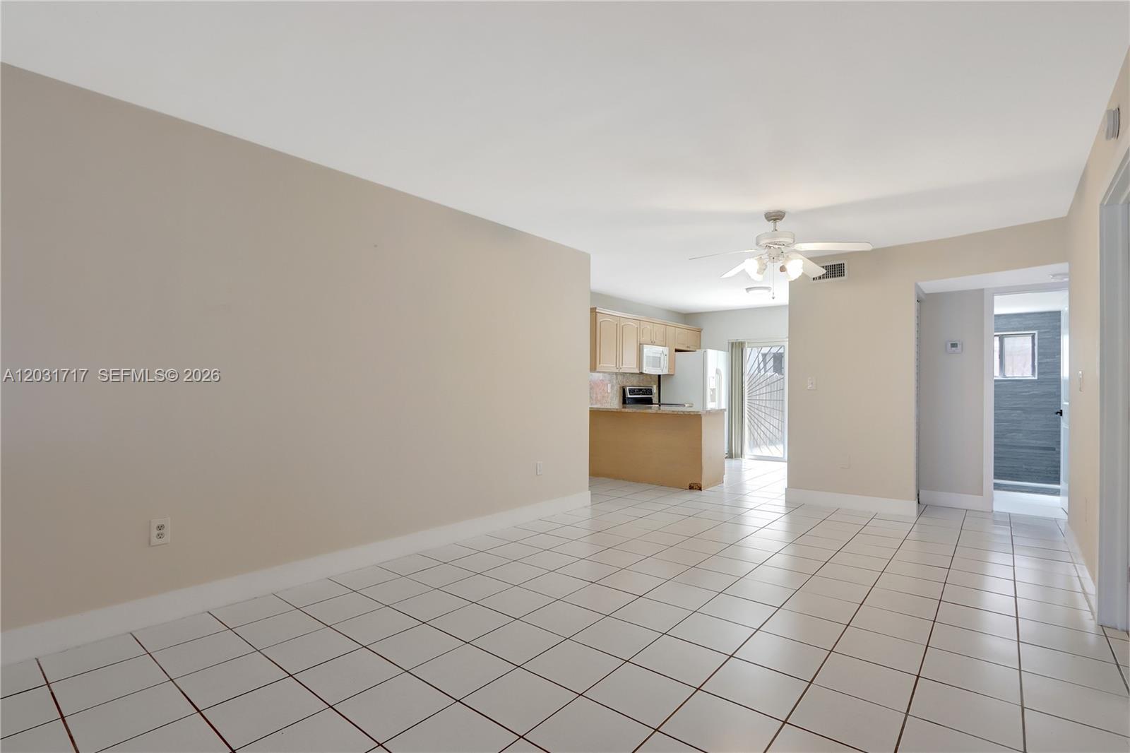 An open-concept living area features white tile flooring, beige walls, and a kitchen with light wood cabinets — 7732 W 29th Way # 102, Hialeah FL 33018, HIALEAH, FL