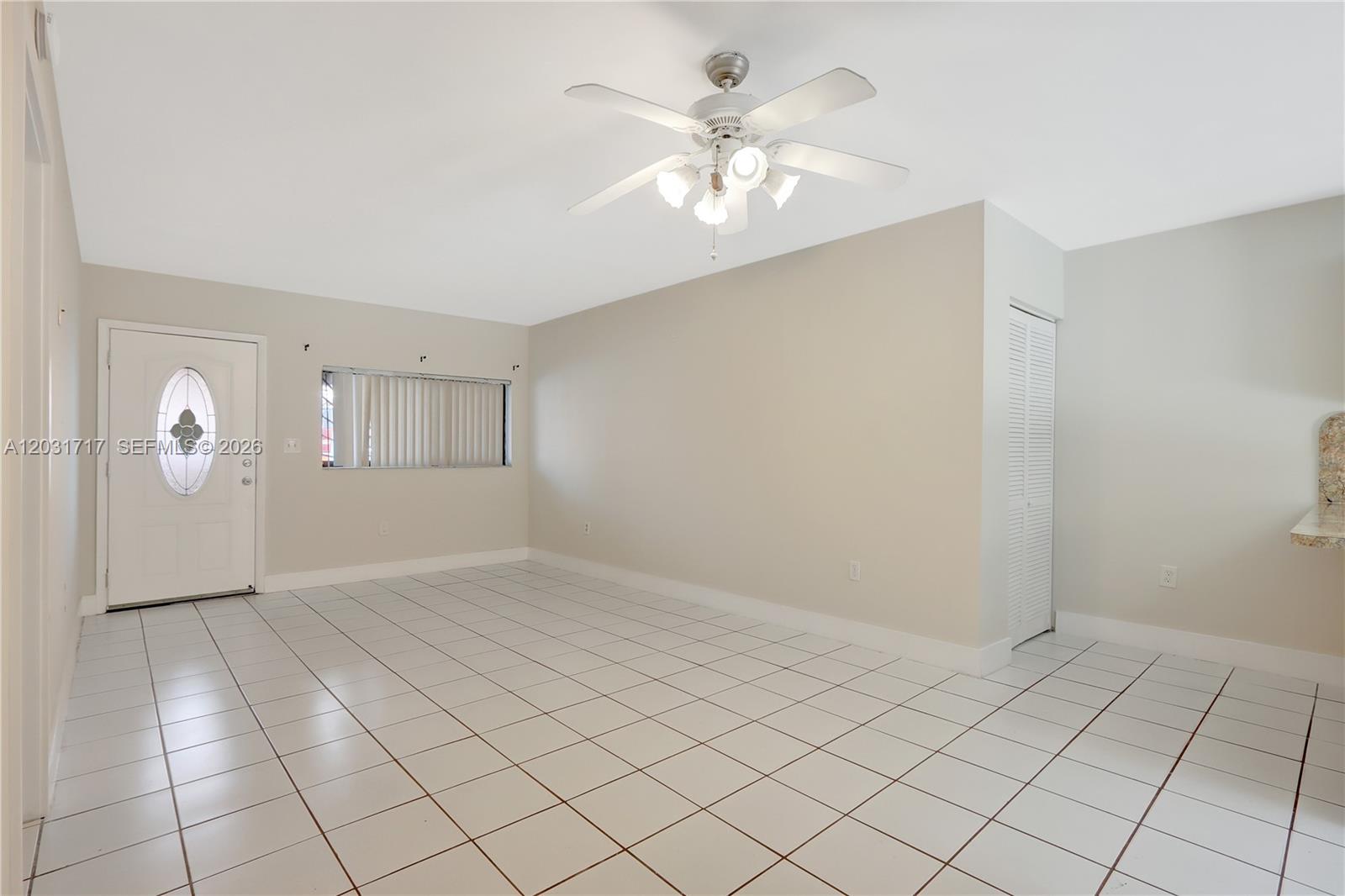 An empty room features white tiled floors, a ceiling fan, and a front entry door — 7732 W 29th Way # 102, Hialeah FL 33018, HIALEAH, FL