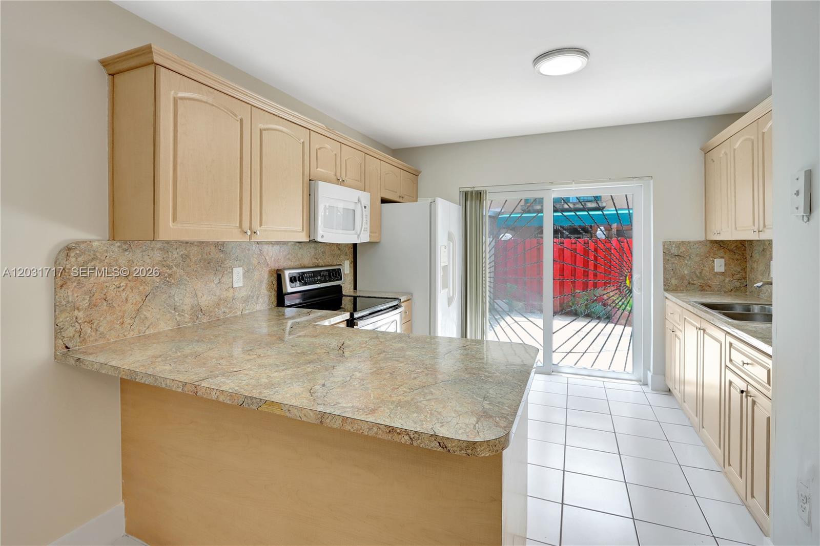A kitchen features light wood cabinets, granite countertops, white appliances, and a sliding glass door — 7732 W 29th Way # 102, Hialeah FL 33018, HIALEAH, FL