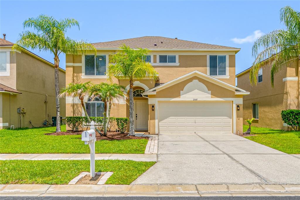 A two-story suburban house with a tan stucco exterior, a two-car garage, and palm trees — 25147 GEDDY DRIVE, LAND O LAKES, FL