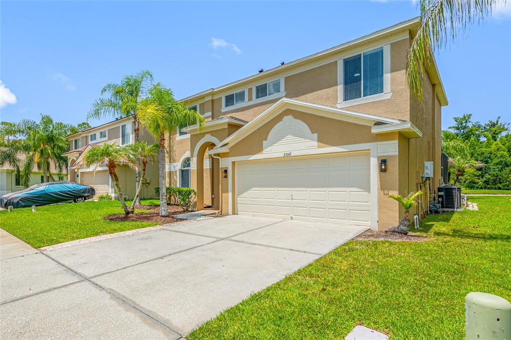 A two-story suburban house with a tan stucco exterior, a two-car garage, and palm trees — 25147 GEDDY DRIVE, LAND O LAKES, FL
