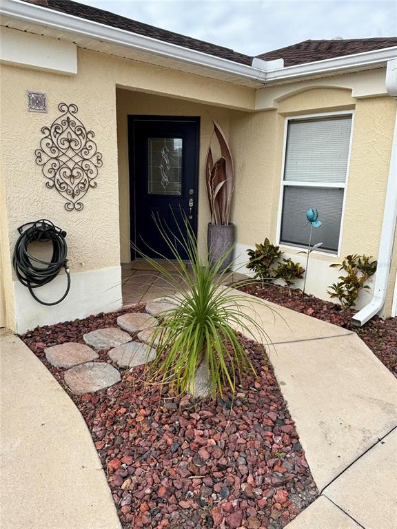 The exterior of a home features a dark front door, a small garden, and a walkway — 1069 BURNETTOWN PLACE, THE VILLAGES, FL