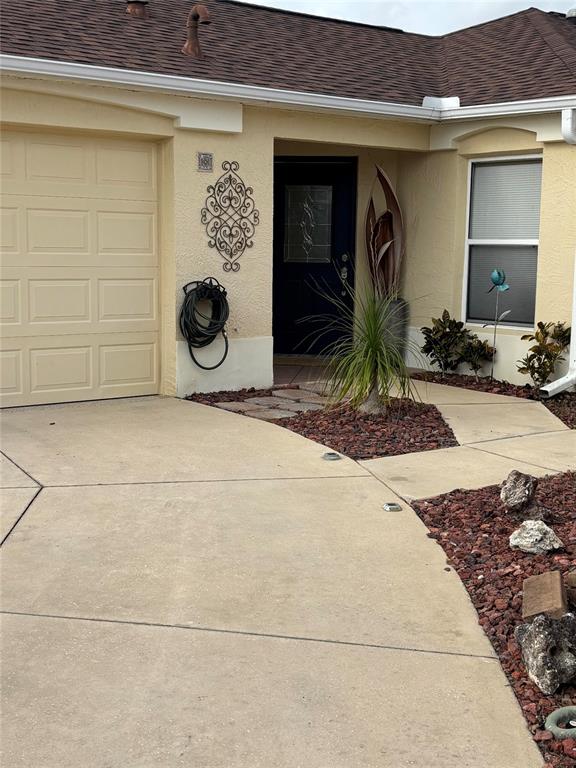 The exterior of a house features a tan garage, a dark front door, and landscaping — 1069 BURNETTOWN PLACE, THE VILLAGES, FL