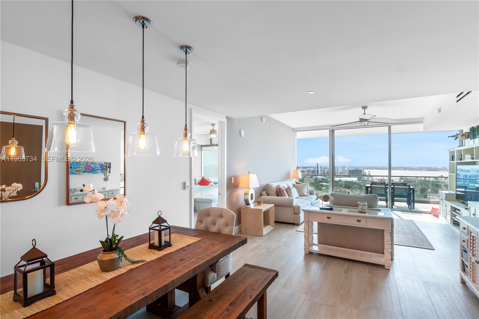 A living room features a white entertainment center, beige sofas, and a balcony with water views — 10201 Collins Ave # 1205, Bal Harbour FL 33154, BAL HARBOUR, FL