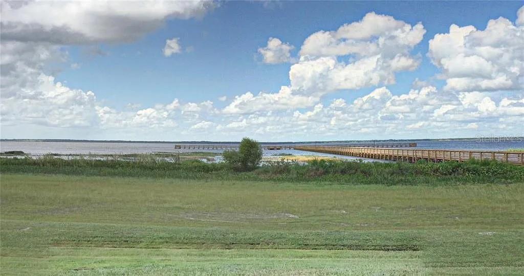 A long wooden pier extends into a large lake under a bright, cloudy sky — 619 CAMELLIA DRIVE, INDIAN LAKE ESTATES, FL
