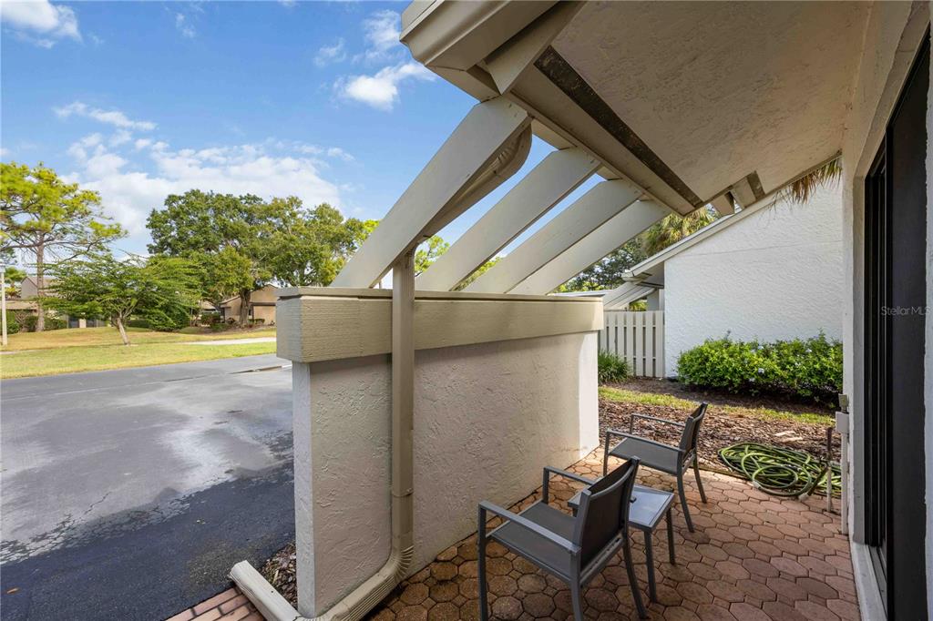 A paved patio with two chairs sits under a slatted roof next to a wall — 5370 MYRTLE WOOD ROAD UNIT 56, SARASOTA, FL