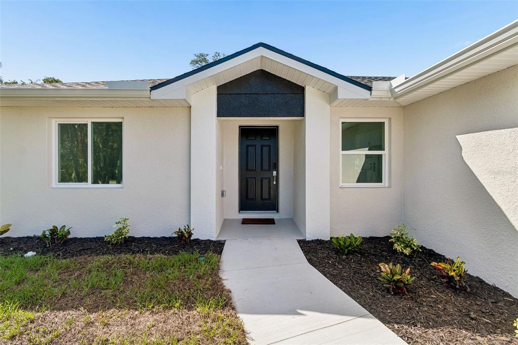 The exterior of a house features a black front door, white stucco walls, and landscaping — 5535 TEVIS TERRACE, NORTH PORT, FL