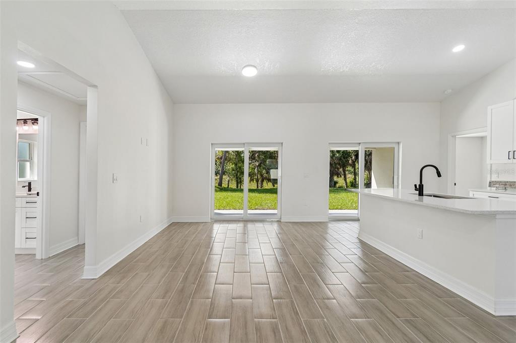 An open-concept living area features light wood-look tile flooring, white walls, and sliding glass doors — 5535 TEVIS TERRACE, NORTH PORT, FL