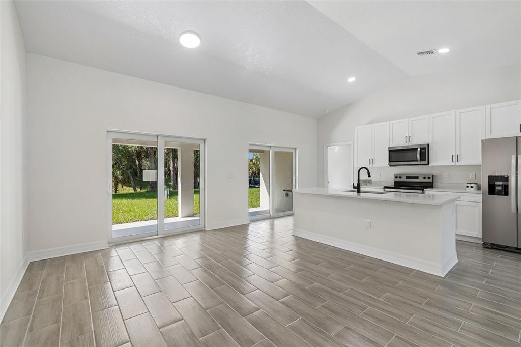 A bright kitchen and living area with white cabinets, stainless appliances, and wood-look tile flooring — 5535 TEVIS TERRACE, NORTH PORT, FL