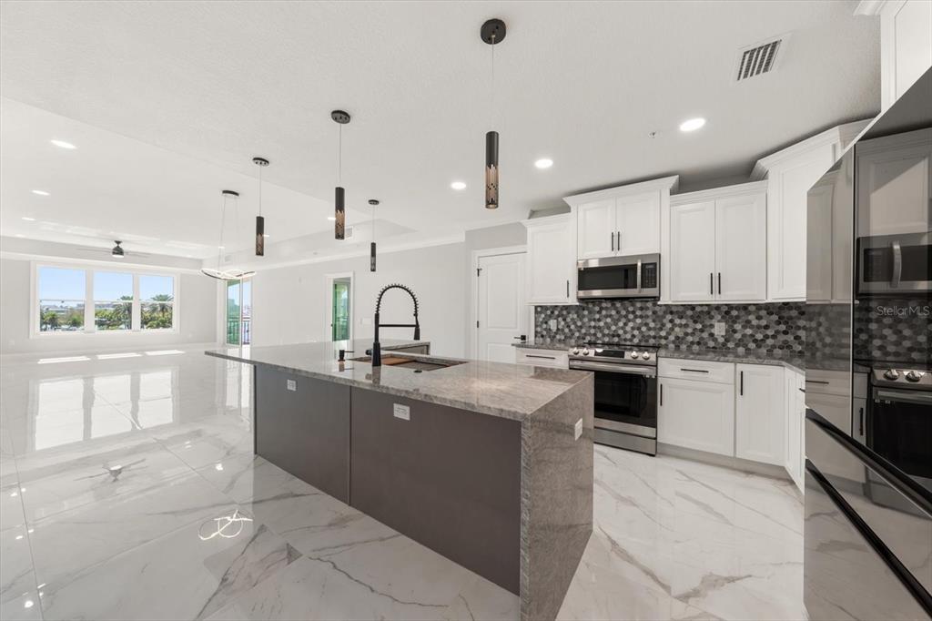 A modern kitchen features a large gray island, white cabinetry, and a hexagonal tile backsplash — 211 DOLPHIN POINT UNIT 303, CLEARWATER, FL