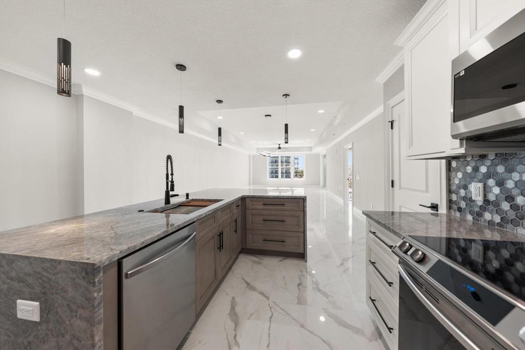 A modern kitchen features gray cabinets, granite countertops, stainless steel appliances, and white marble flooring — 211 DOLPHIN POINT UNIT 303, CLEARWATER, FL