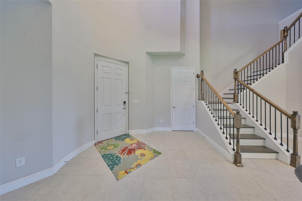 A bright foyer features light tile flooring, a white front door, and a wooden staircase — 11909 CLIMBING FERN AVENUE, RIVERVIEW, FL